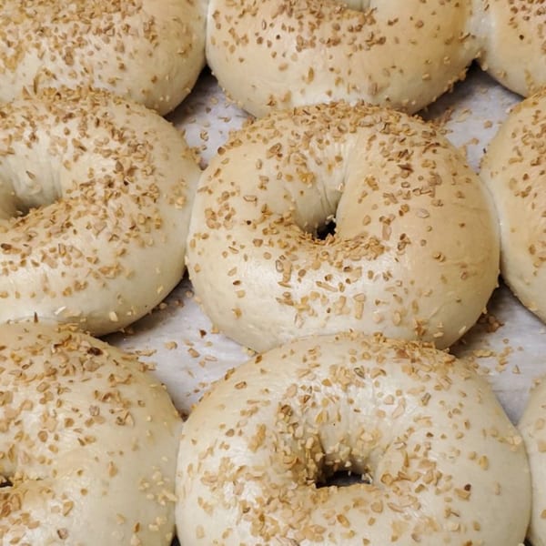 Close-up of several freshly baked bagels from Alicea's NY Bagels & Subs, topped with sesame seeds.
