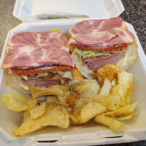 Two hearty Alicea's NY Bagels & Subs sub-sandwiches, overflowing with meats and toppings, served with potato chips.