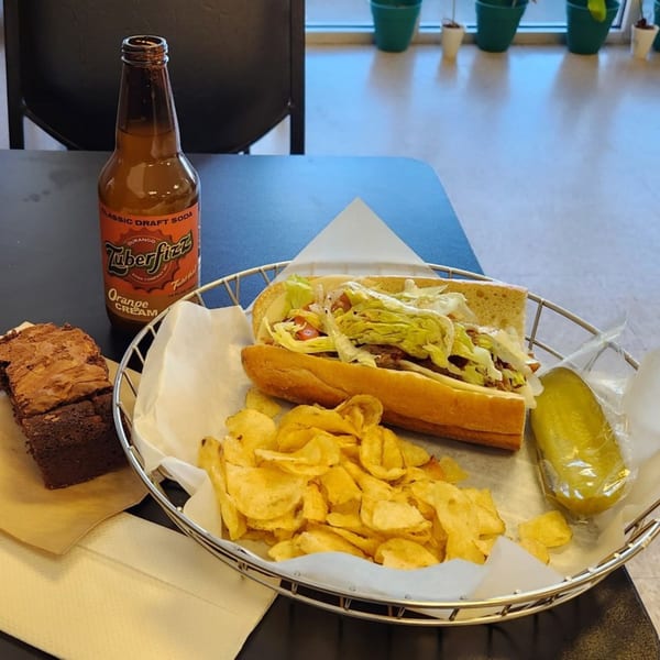 Alicea's NY Bagels & Subs sub-sandwich meal with chips, pickle, soda, and brownie on a table.