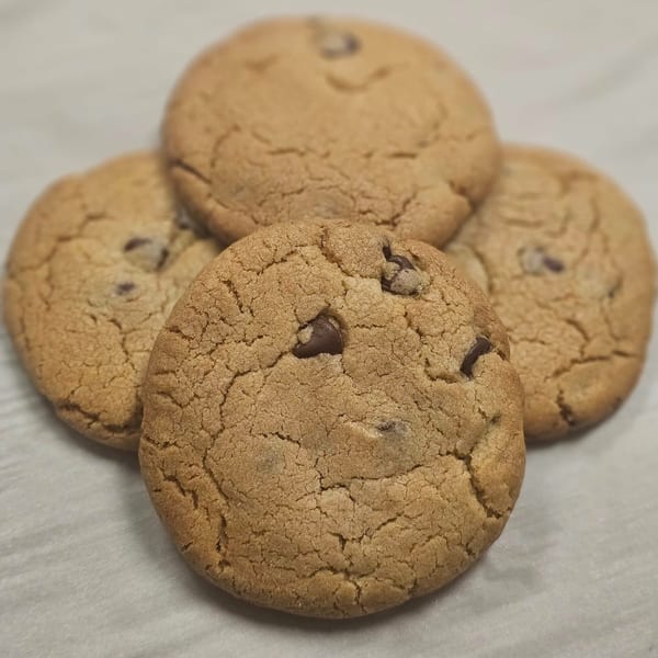 Four freshly baked chocolate chip cookies arranged in a clover shape on a light surface.